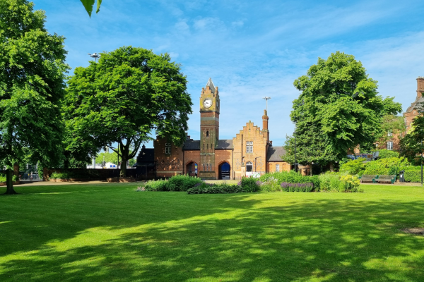 Walsall Arboretum clock tower, a red brick Victorian building with grass in front, trees surrounding it and a blue sky above