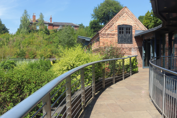 Walsall Arbortetum visitor centre, showing a red brick Victorian building surrounded by shrubs, with a modern extension