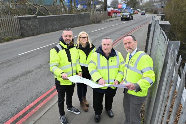 A group of 4 people in high vis jackets stand by a road looking at a map