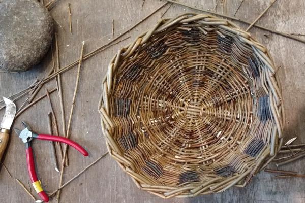 Handmade willow basket with basket-making tools on a table