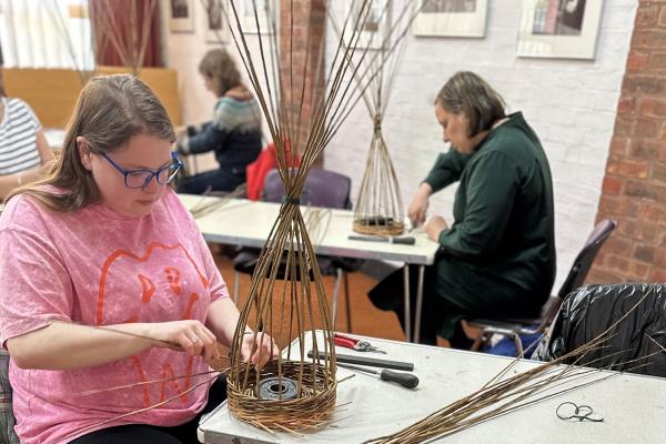 people hand weaving baskets in a workshop