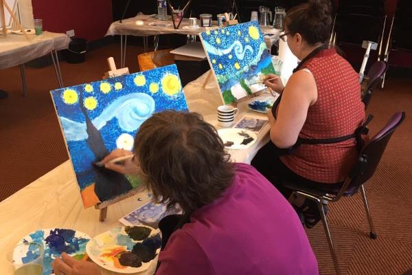 Two people painting their own versions of Starry Night in a workshop