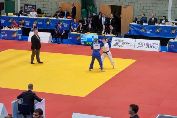 A high angle view of a Judo cup event, the floor is marked out with three large yellow squares and two people in judo kit take part