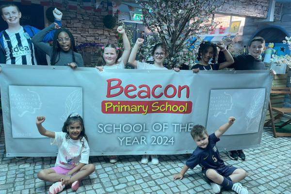 Image depicts children from Beacon Primary School holding a banner to celebrate School of the Year.