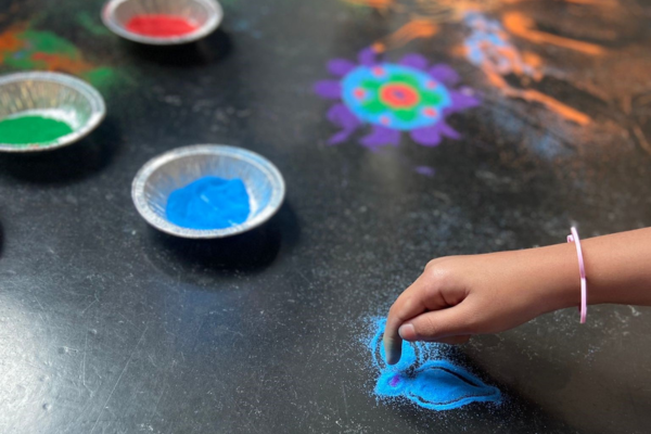 A hand creates patterns from multicoloured sand