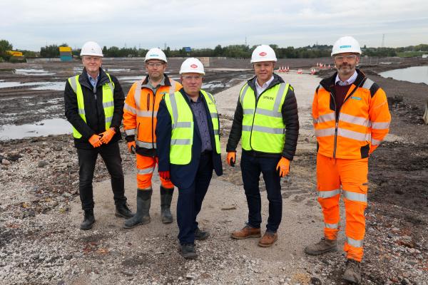 A group of people in high vis and hard hats stand together on a construction site smiling at the camera