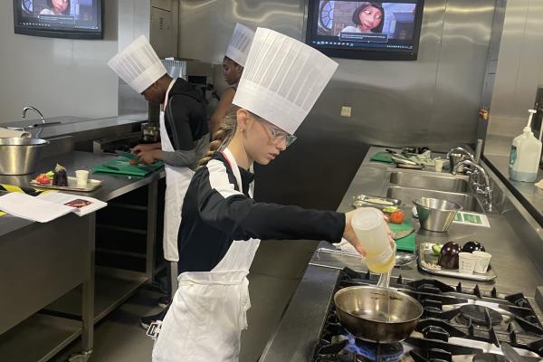 Image depicts a young person pouring an ingredient into a cooking pan.