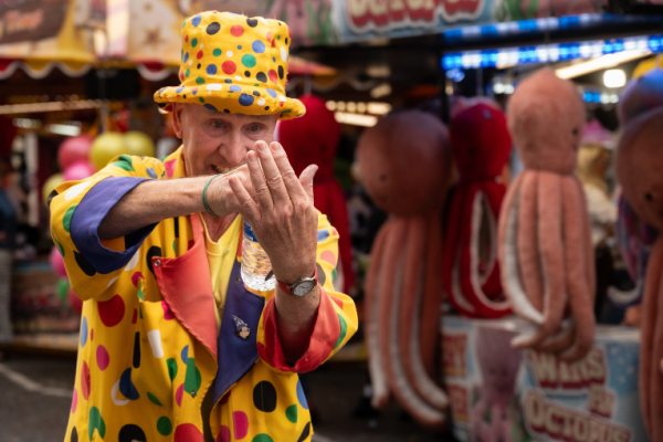 A children's entertained dressed in bright spotty clothes and wearing a top hat.