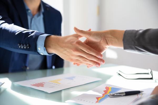 Two people shaking hands across a desk top in an office environment