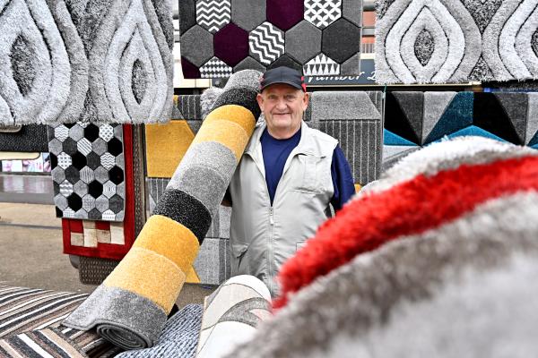 A smiling trader at their stall on Bloxwich Market surrounded by rolled up rugs