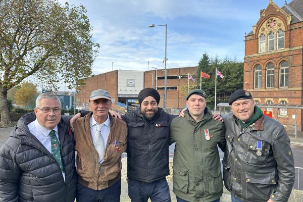 Image depicts five veterans with the Saddlers Centre and British and Sikh flags in the background.