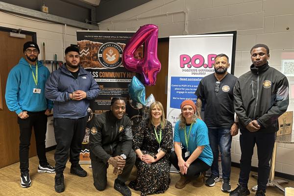 Image depicts seven representatives from Bloxwich Community Partnership and Midland Langar Seva Society in front of two banners and a number 4 balloon.