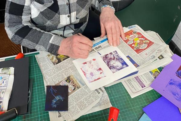 Close up of the hands of a person who is creating prints from a lino tile.