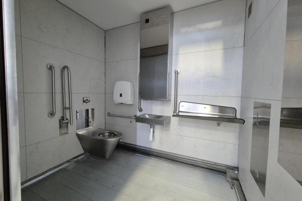 Inside a modern public toilet stall, the furniture is stainless steel and the walls and floor are grey