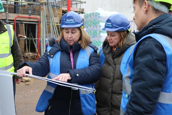 Two ladies in blue high-vis jackets and hard hats look at a site plan