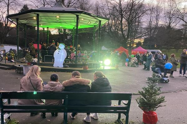 Image depicts a family sitting on a bench watching bandstand performances.