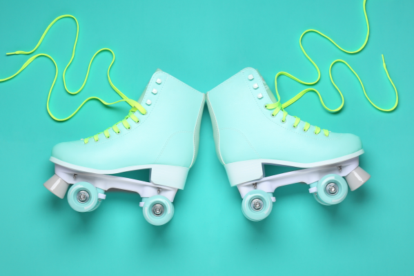 Pale blue roller skates with yellow laces lying flat on a darker turquoise background