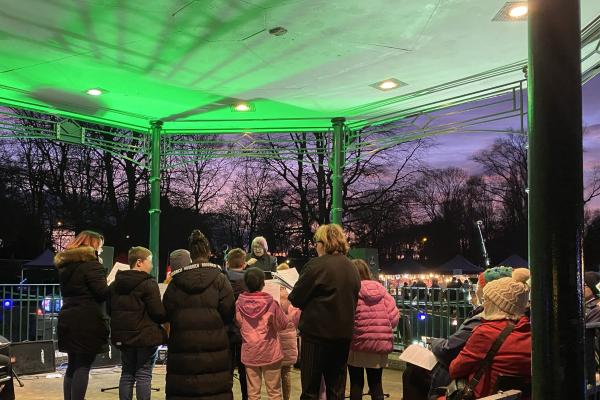 Image depicts a group of school children from behind singing at the bandstand at Willenhall Memorial Park.