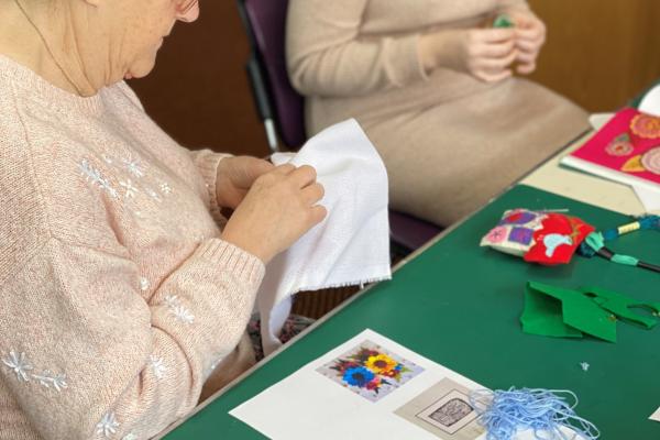 Craft materials on a table, and the hands of two people sewing