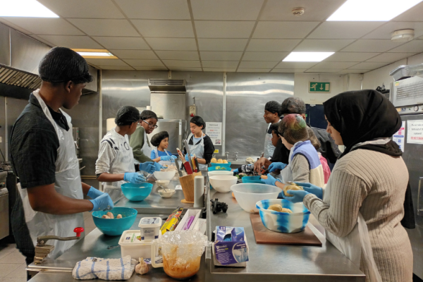 Image depicts a group of children and young people preparing food in a professional kitchen.