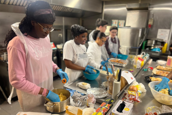 Image depicts a group of children and young people preparing food in a professional kitchen.