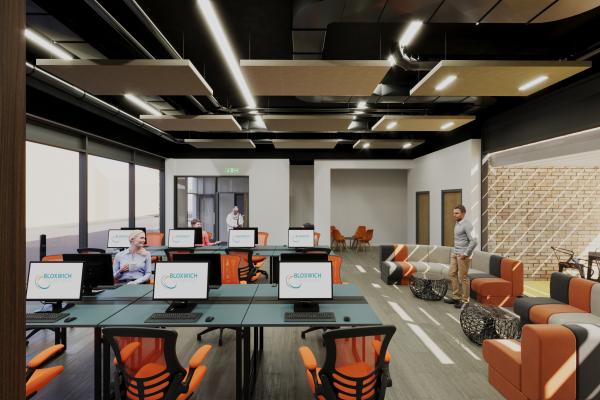 A bright modern office space with orange and grey seating and a bank of computers