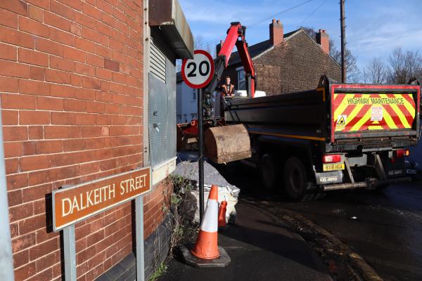 Crane lorry clearing waste from street with Dalkeith Street sign