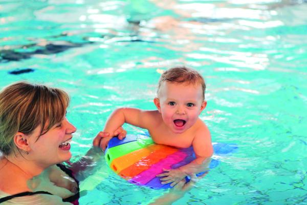 female and baby in a swimming pool with a rainbow coloured float 