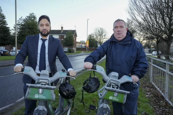 Two councillors stand with bicycles on the grass of a central reservation on a dual carriageway