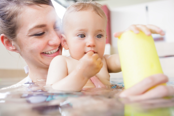 female and baby in an indoor swimming pool baby is holding a yellow woggle float