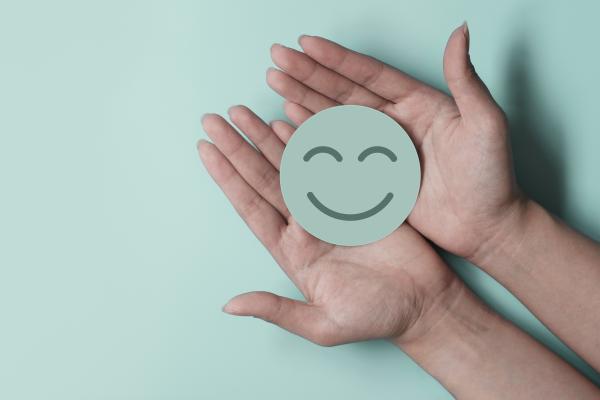 Green disc with smiley face on it, held in two open hands on a pale green background.