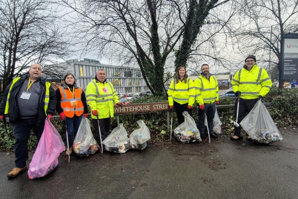 a group of 6 people in high vis jackets holding bags of litter stand around a street sign that says Whitehouse Street