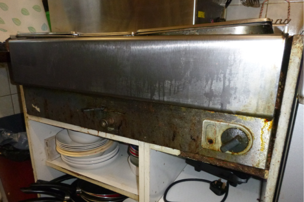 Image shows dirty / greasy bain marie sitting on deteriorated shelving in kitchen.