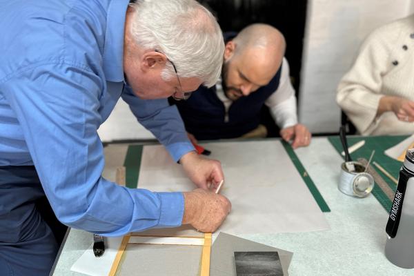 Two people cutting bookbinding materials at a small table.