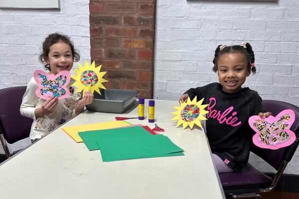 Two young children holding artworks of paper flowers they have made