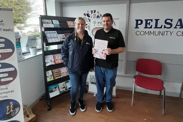 Image depicts a man and woman with a sticker and poster for breastfeeding friendly scheme.