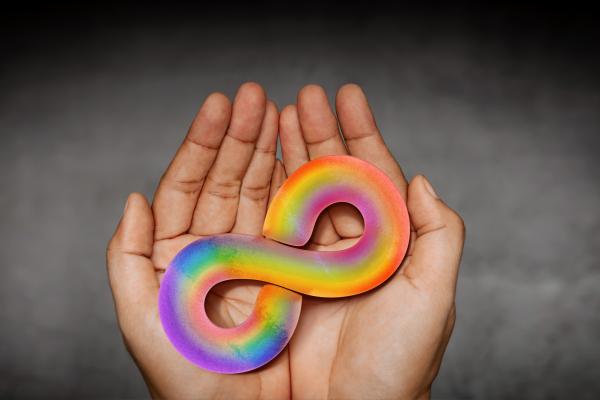 hands holding an autism awareness rainbow infinity symbol