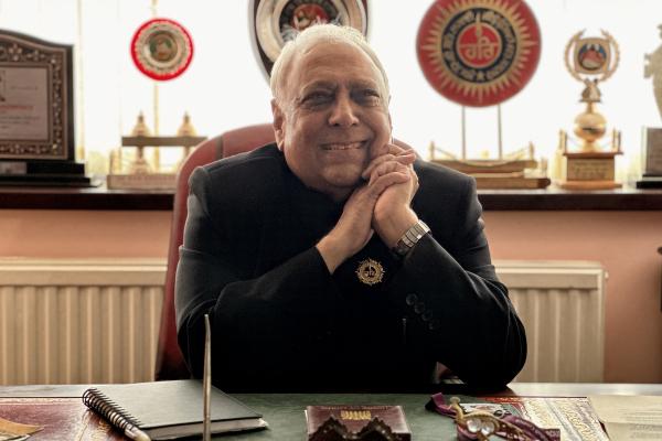 Image depicts Councillor Ram. K. Mehmi MBE smiling at his desk with his hands together on the side of his face.