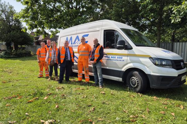 A group of people stand in front of a van wearing high vis jackets