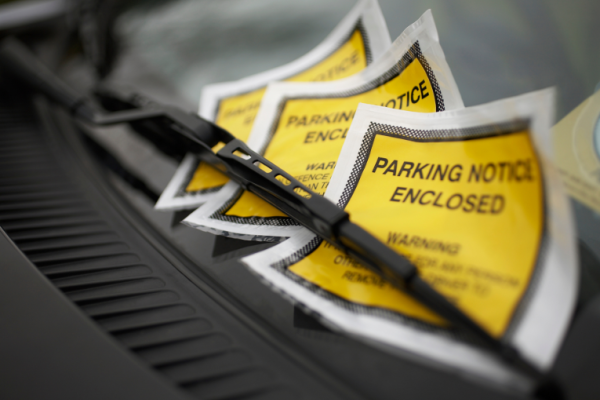 Image depicts three parking charge notices under a windscreen wiper of a car.