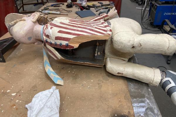 A wooden model of a man laying on its side on a work bench