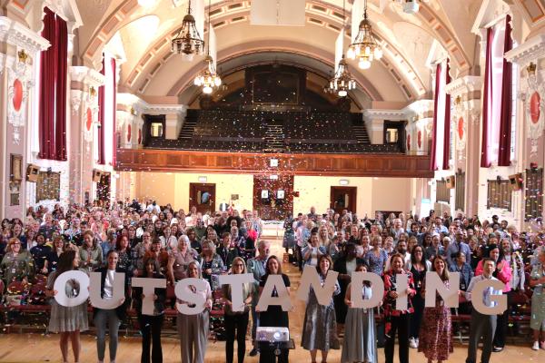OUTSTANDING  white letters with hundreds of people cheering and confetti