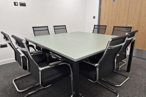 A modern new meeting room with a large square table and 8 black chairs