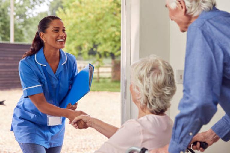 Carer arriving at house to give care to lady in wheelchair, with relative close by.